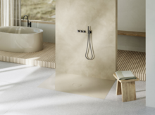 Salle de bains lumineuse avec douche à l’italienne, baignoire autoportante au fond, banc en bois et tabouret avec livre.